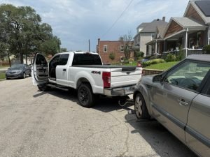White 4x4 tow truck preparing to tow silver SUV on residential street