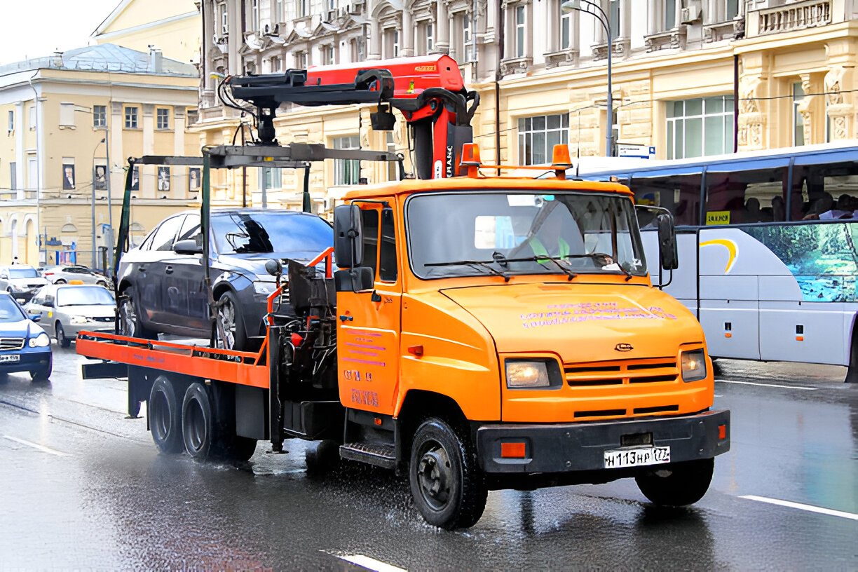 Orange Zil 5301 Bychok tow truck carry a broken car at the city street.